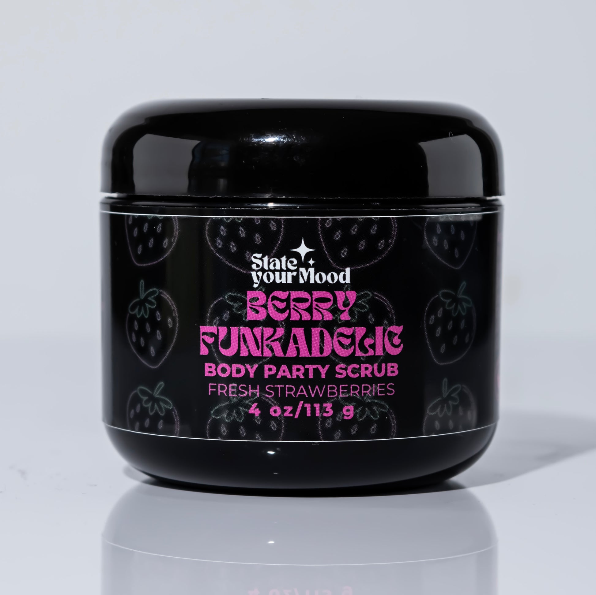 A black jar of 'Berry Funkadelic Body Party Scrub' from the State Your Mood brand. The label features a playful, bold pink font with the scent description 'Fresh Strawberries' written below. The background of the jar is decorated with subtle outlines of strawberries, complementing the product's theme. The jar contains 4 oz (113g) of body scrub, and the reflection of the jar can be seen on the glossy white surface beneath it, creating a clean and modern look.